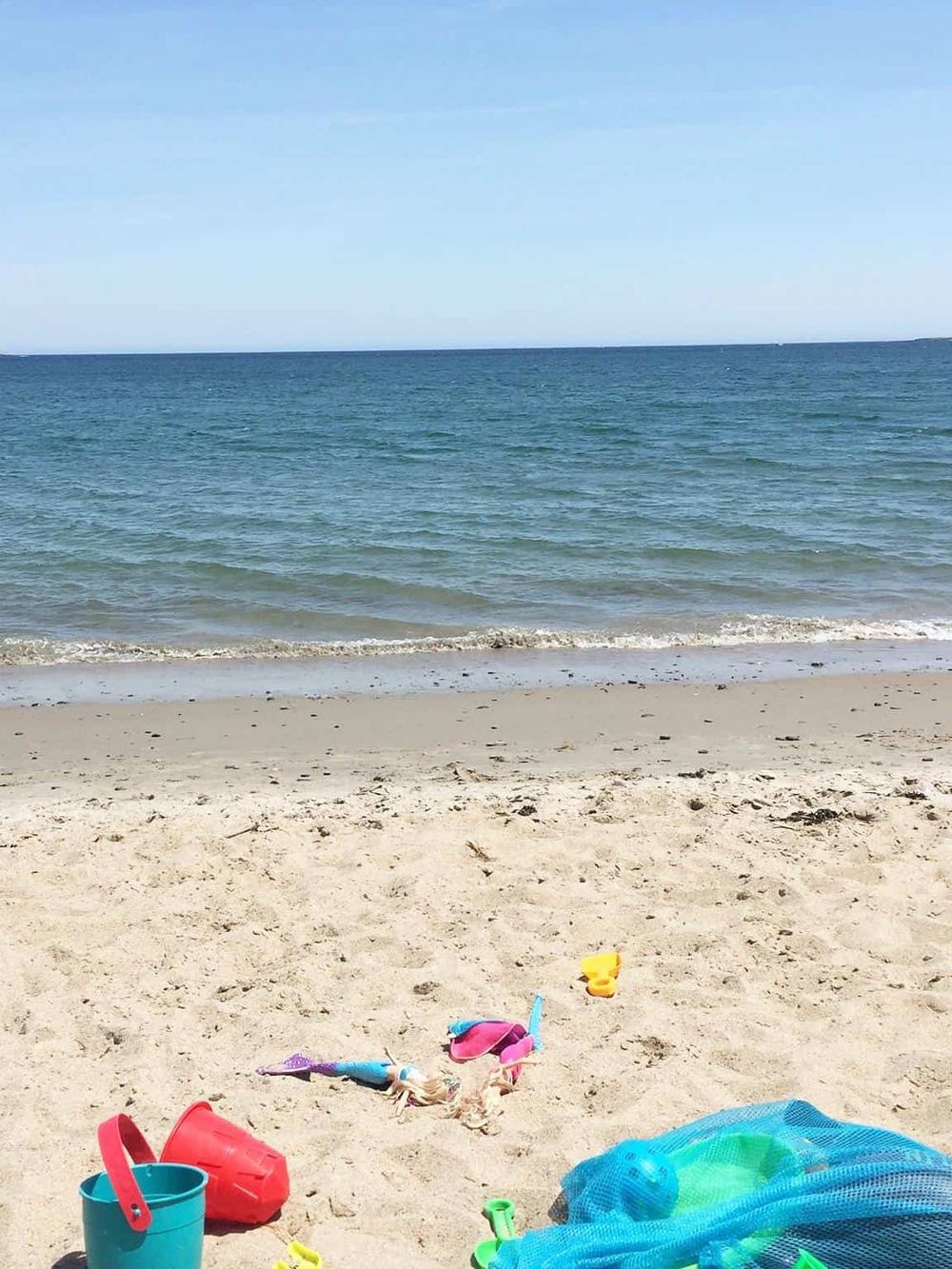 Colorful beach toys and sand toys on a sandy shore with ocean waves and blue sky in the background.