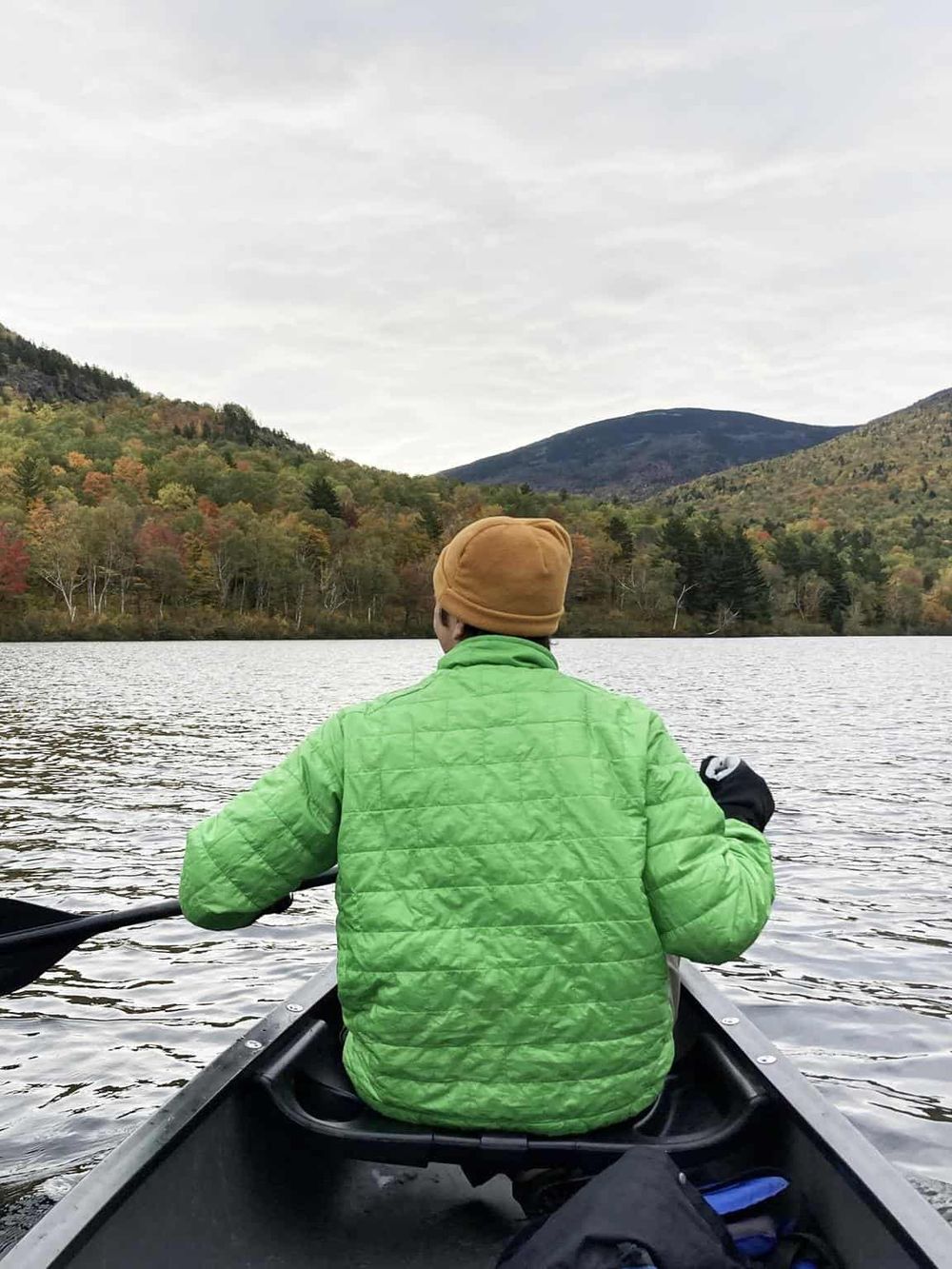 Serene kayak paddle on a tranquil lake surrounded by autumn foliage and mountains.