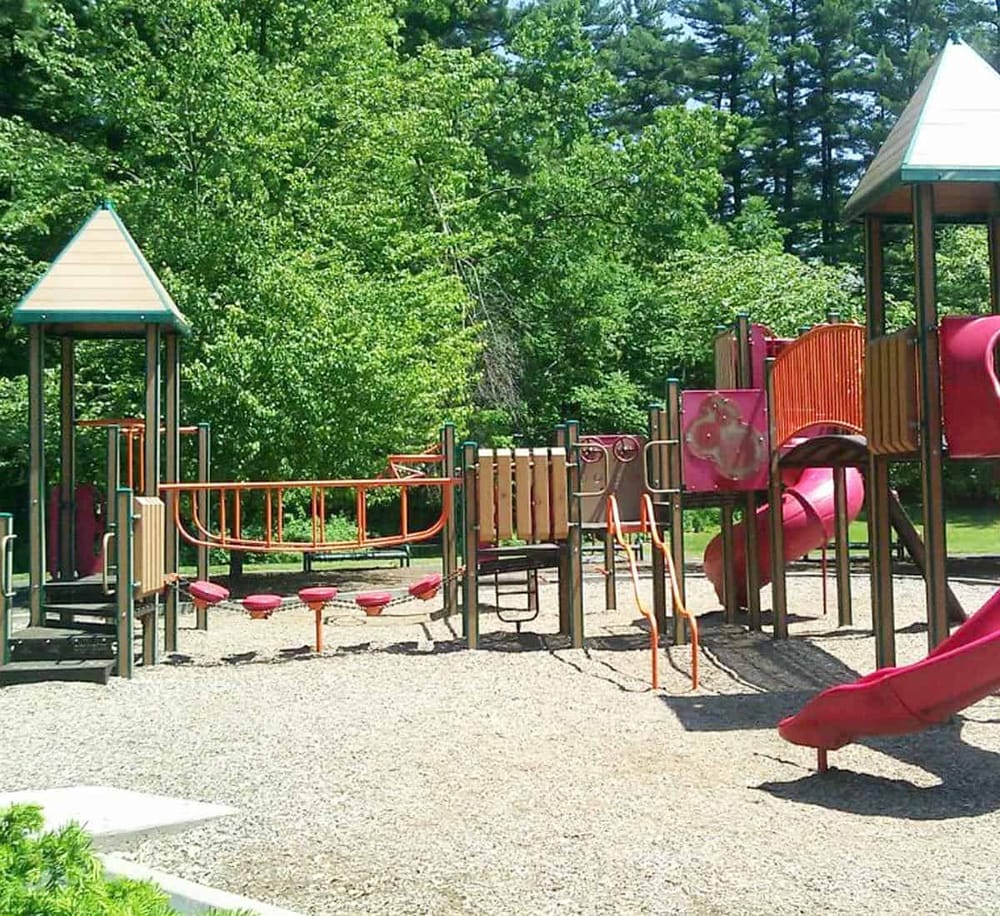 Colorful children's playground set with slides and climbing structures in a park with lush green trees.