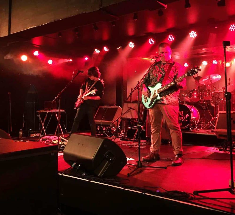 Live music performance at QuestForDirections event, showcasing talented musicians on stage with vibrant red lighting.