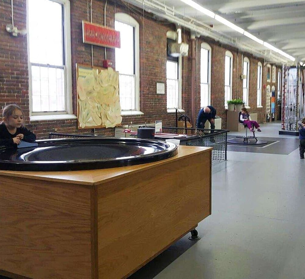 Colorful art exhibit in a spacious industrial-style gallery with children and adults exploring interactive exhibits.