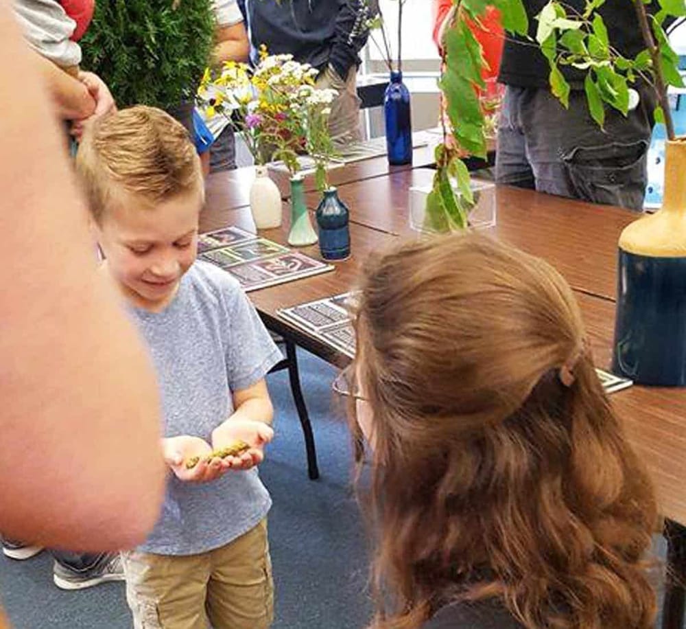 Bright young boy showing a green object to a woman at a family-friendly event organized by QuestForDirections, featuring vibrant flowers and decorative vases.