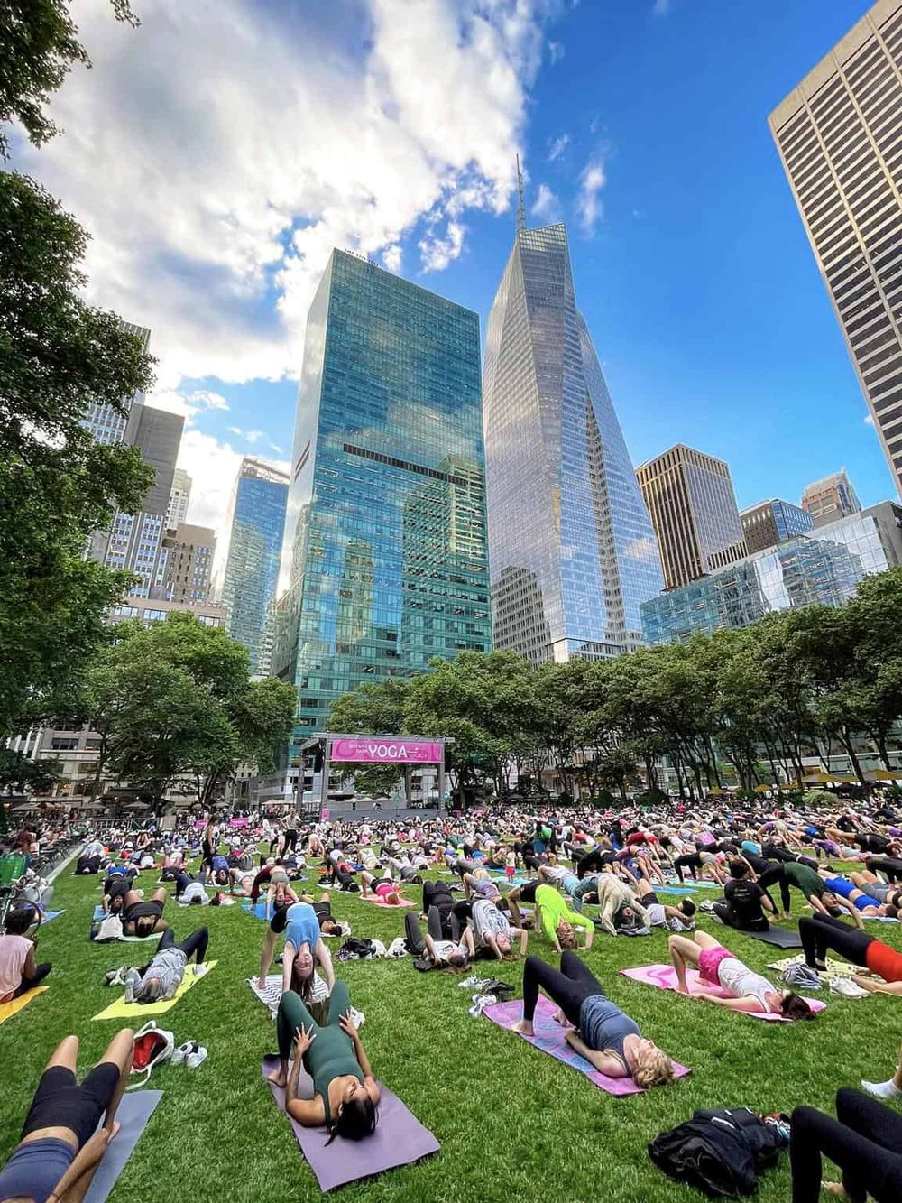 People doing yoga outdoors in city park with skyscrapers in the background, fitness, wellness, community, urban yoga class, healthy lifestyle, QuestForDirections.