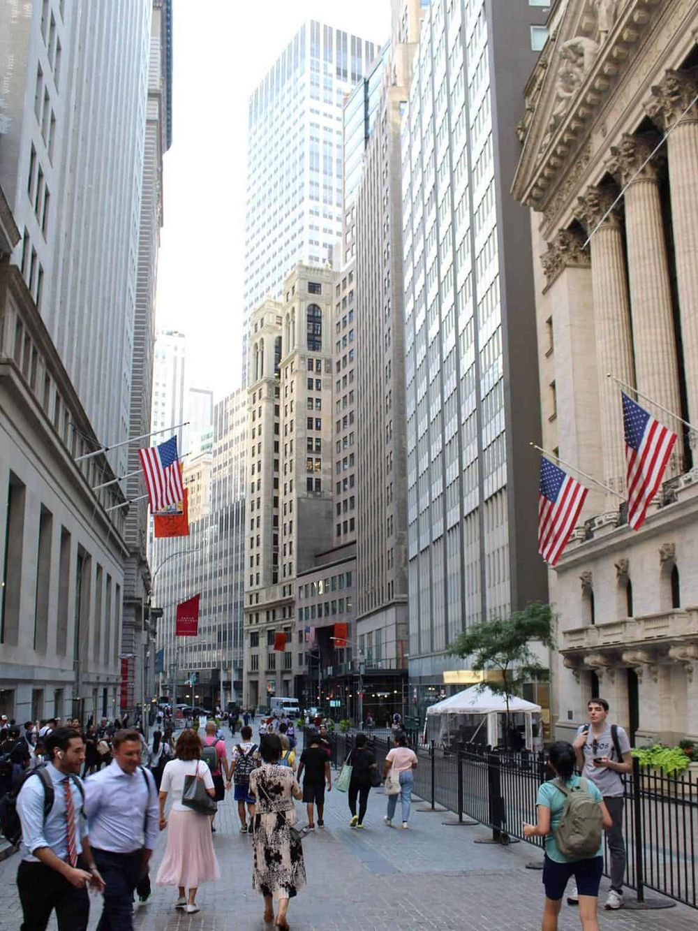 Downtown street scene in New York City with people walking among skyscrapers and American flags.
