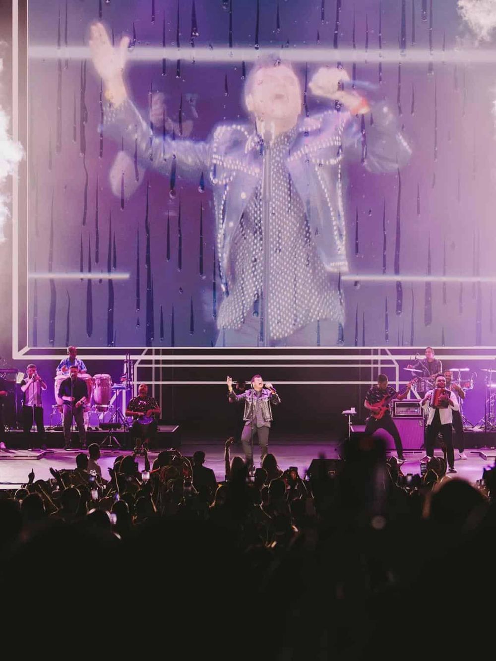 Vibrant concert scene with performers dancing on stage, large digital display, and lively audience engagement.