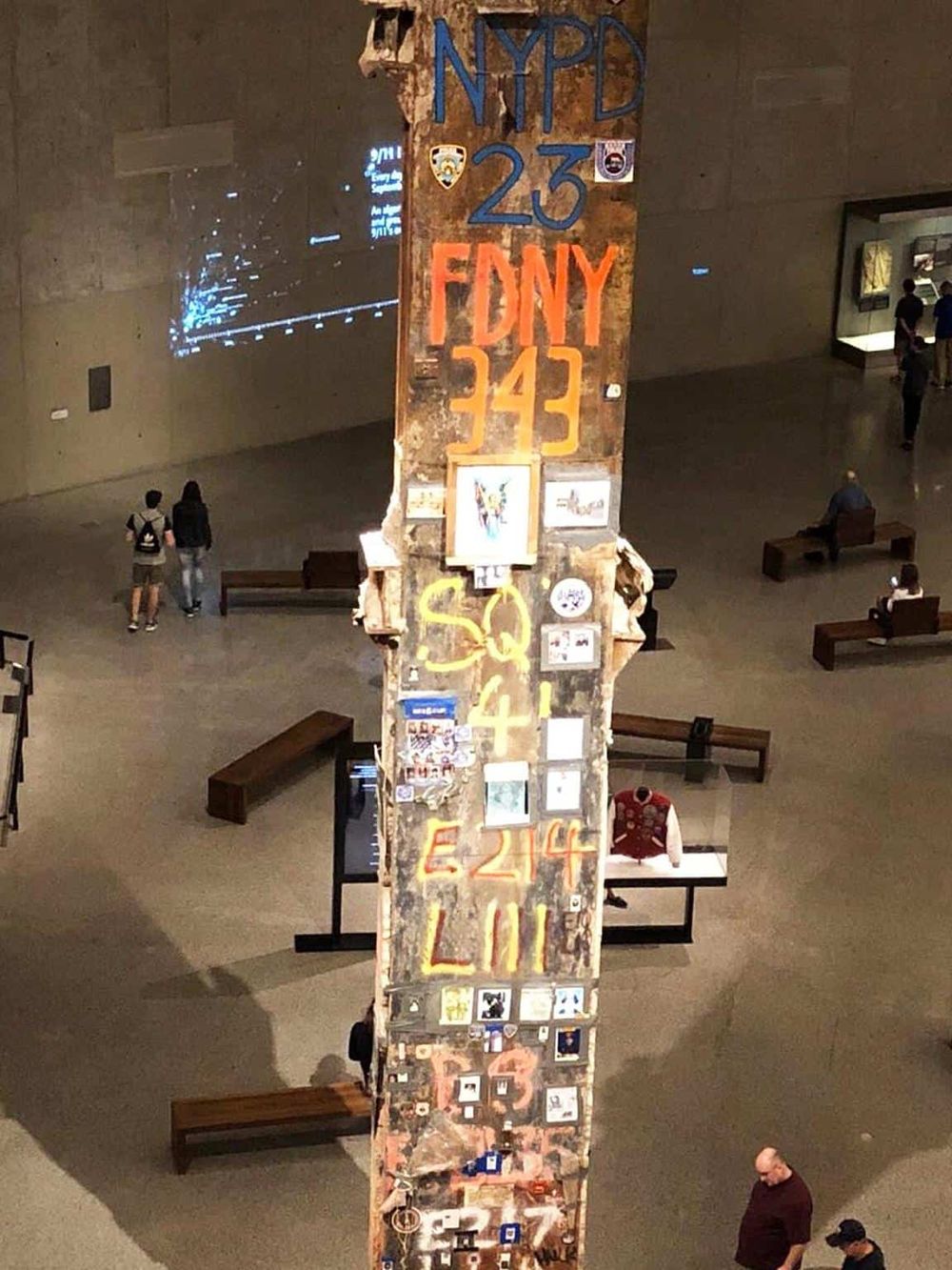 Graffiti-covered wall with emergency numbers at a museum exhibit, featuring NYPD, FDNY, and other city services.