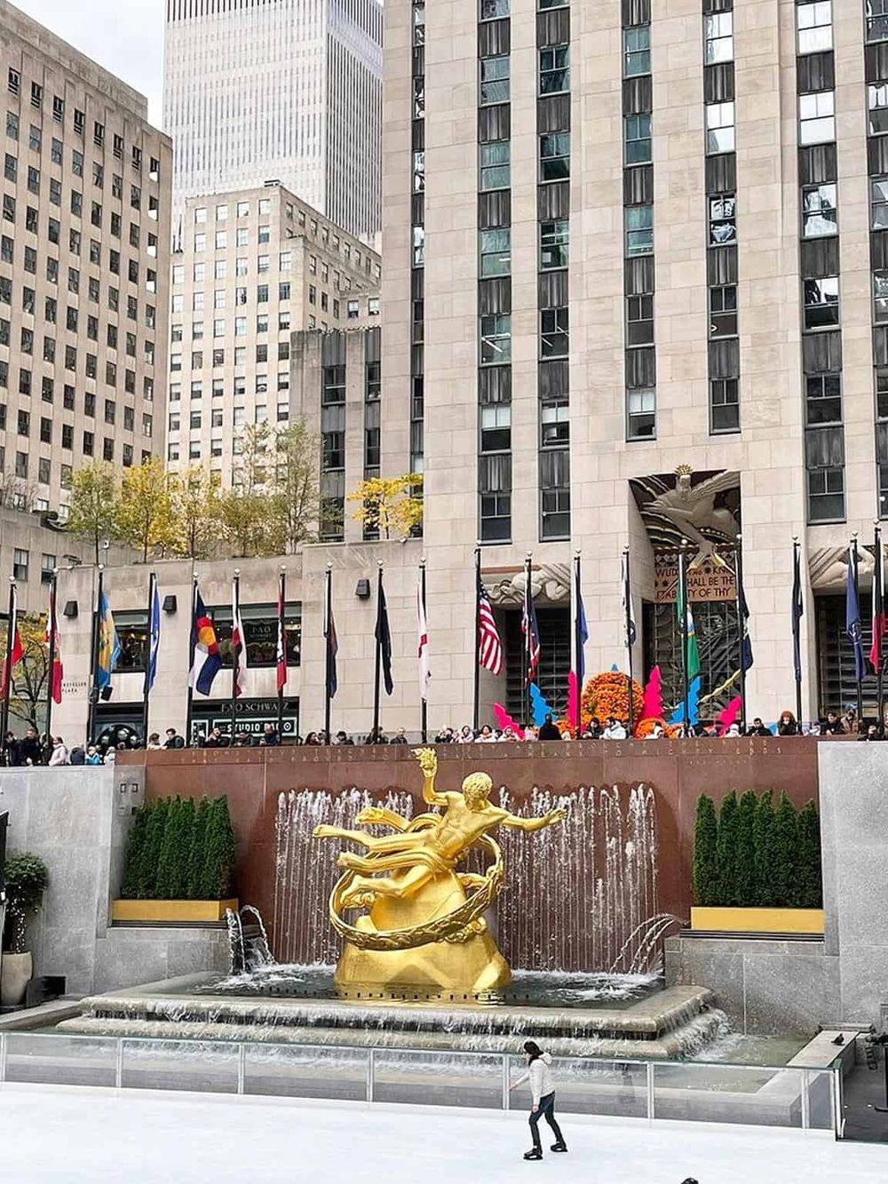 Colorful flags and a golden statue fountain outside Rockefeller Center in New York City.