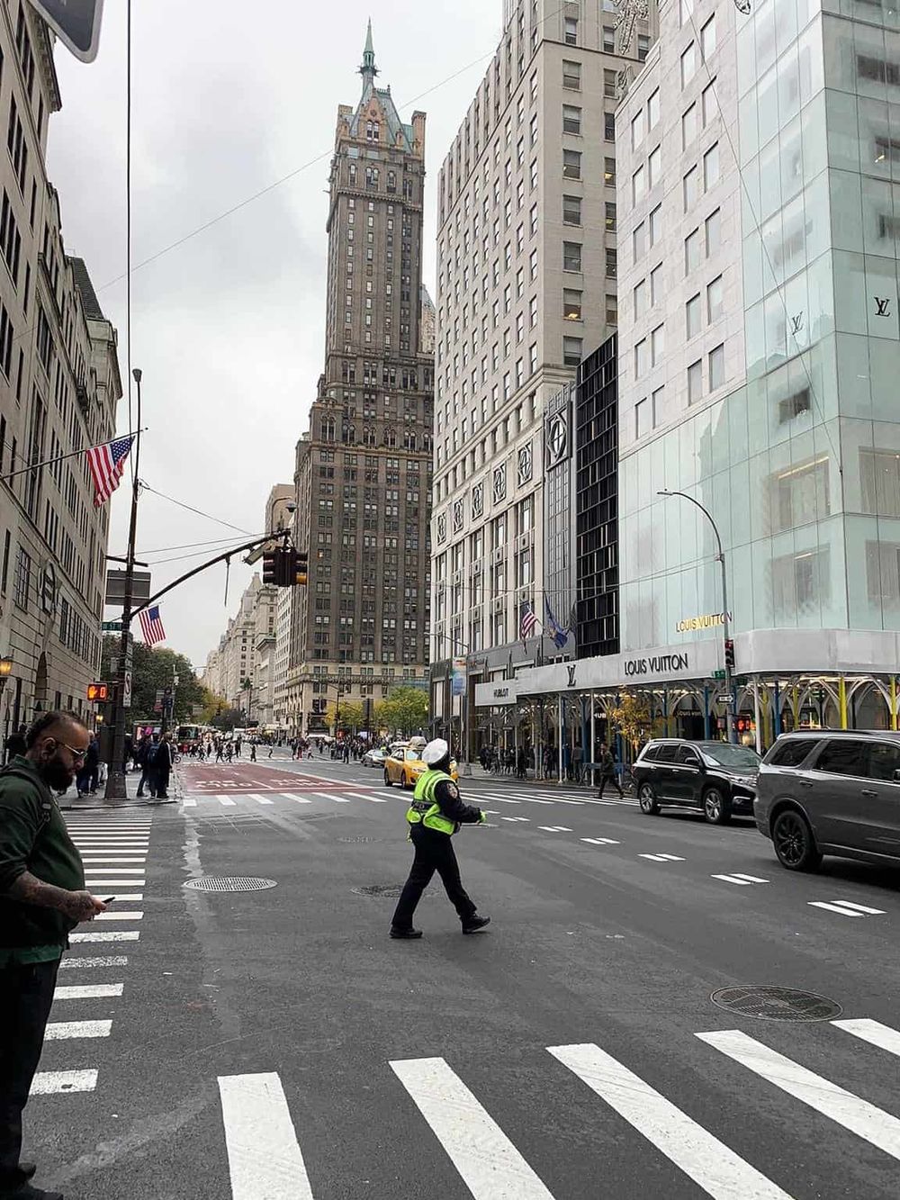 People crossing a busy urban intersection in front of Louis Vuitton store and historic skyscraper.