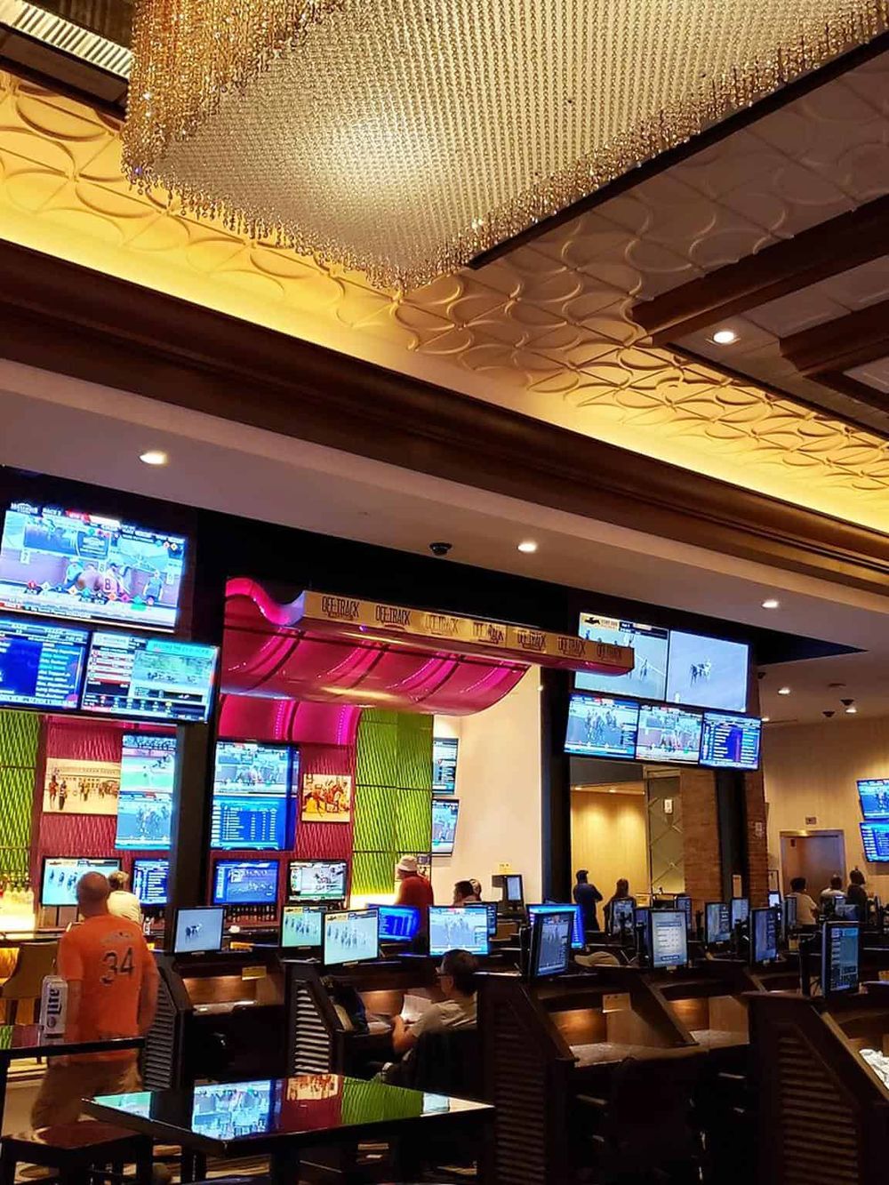 Bright sports betting lounge with multiple screens displaying horse racing, betting odds, and live events.