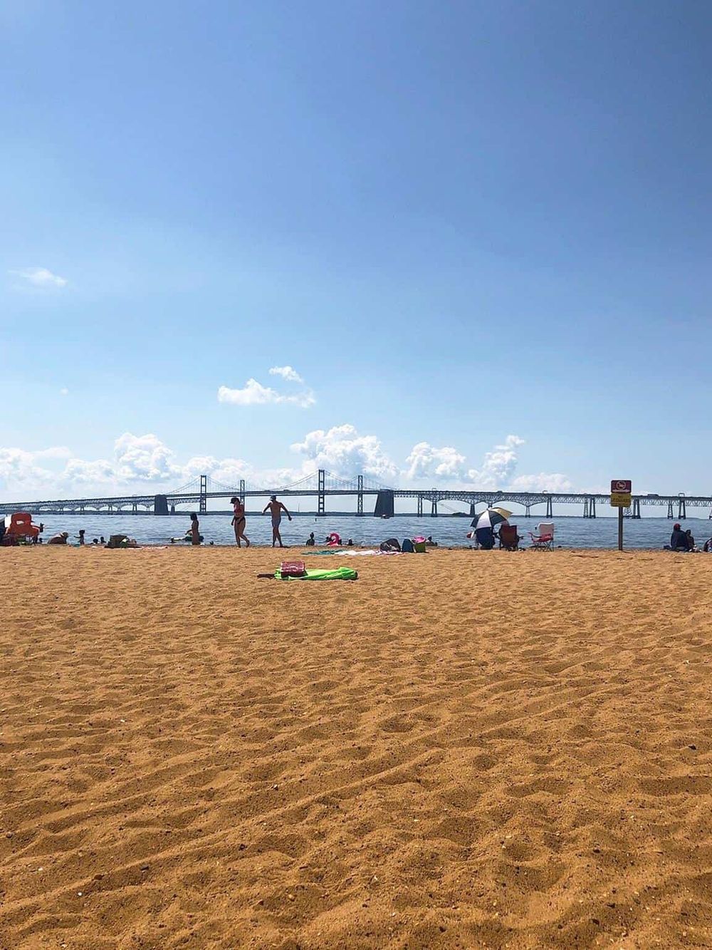 Beach with people, bridge in the background, sunny day, QuestForDirections travel destination SEO.