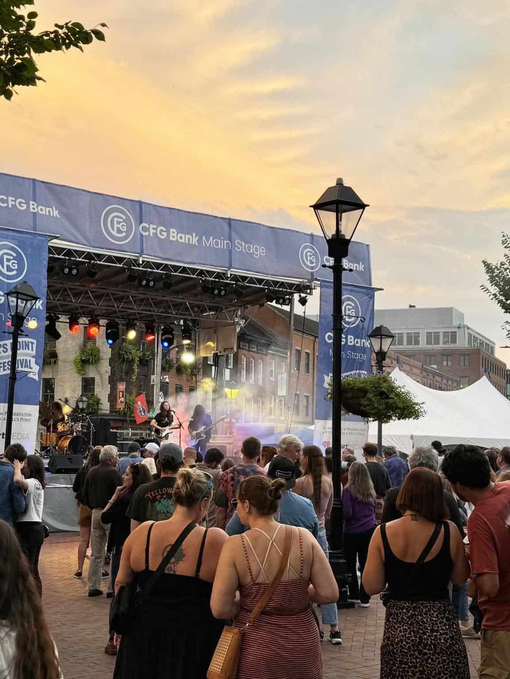 Live outdoor music concert with a crowd at sunset in downtown, promoting local events and community engagement.