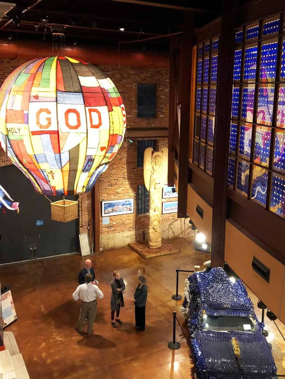 Colorful hot air balloon art with "GOD" inscription in an indoor museum setting.