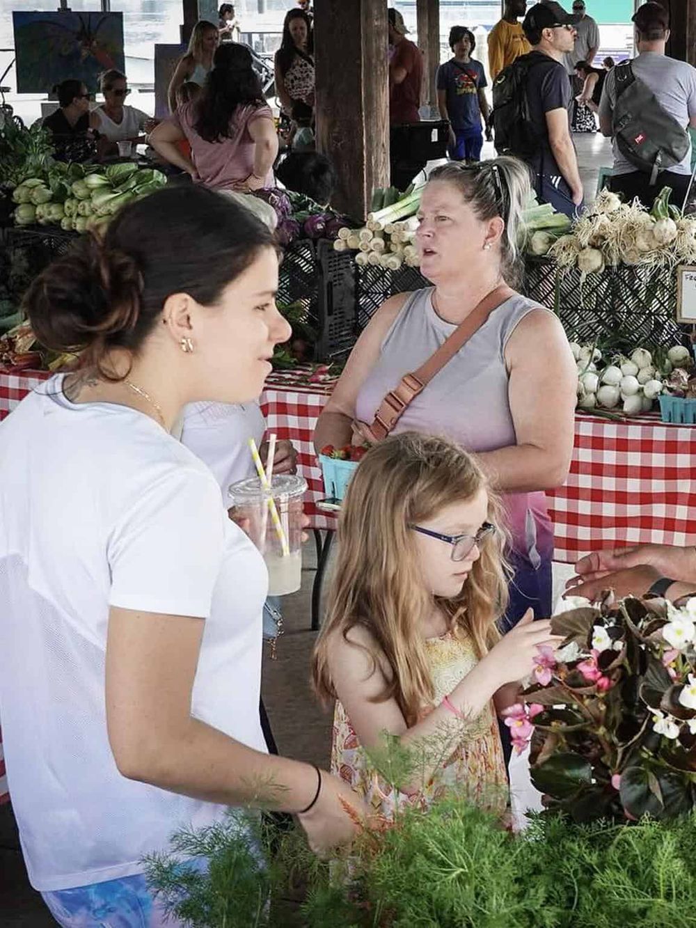 Fresh produce market scene at QuestForDirections. People shopping for vegetables and flowers at an outdoor farmer's market.