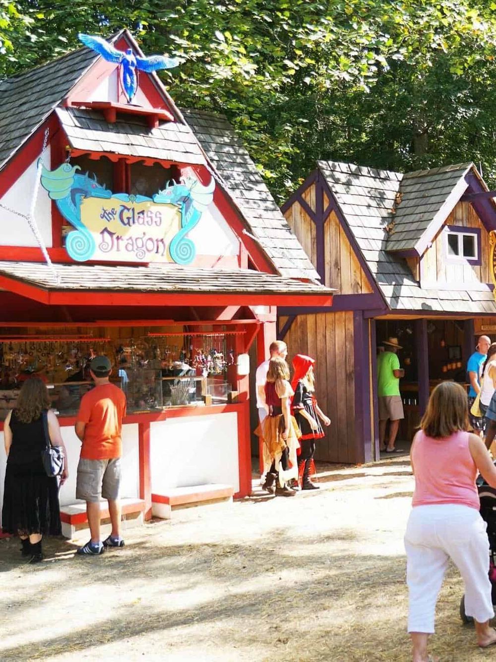 Colorful fairy tale-themed shop at Quest for Directions, surrounded by visitors in a whimsical outdoor village setting.