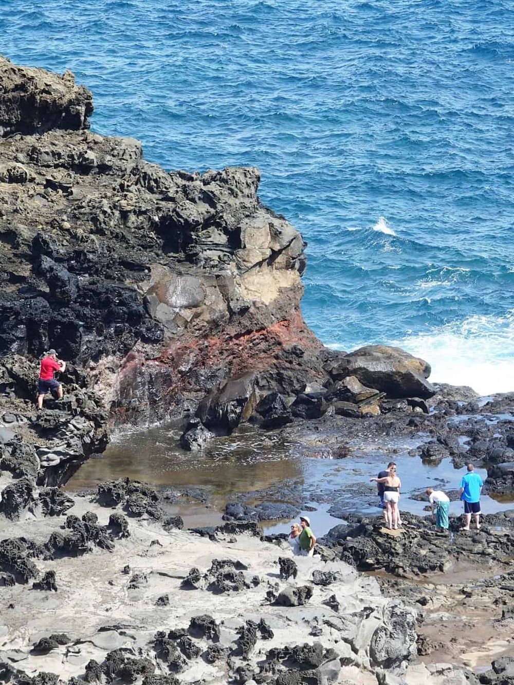 Scenic rocky seaside with people exploring ocean tide pools and taking photos on rugged coast.