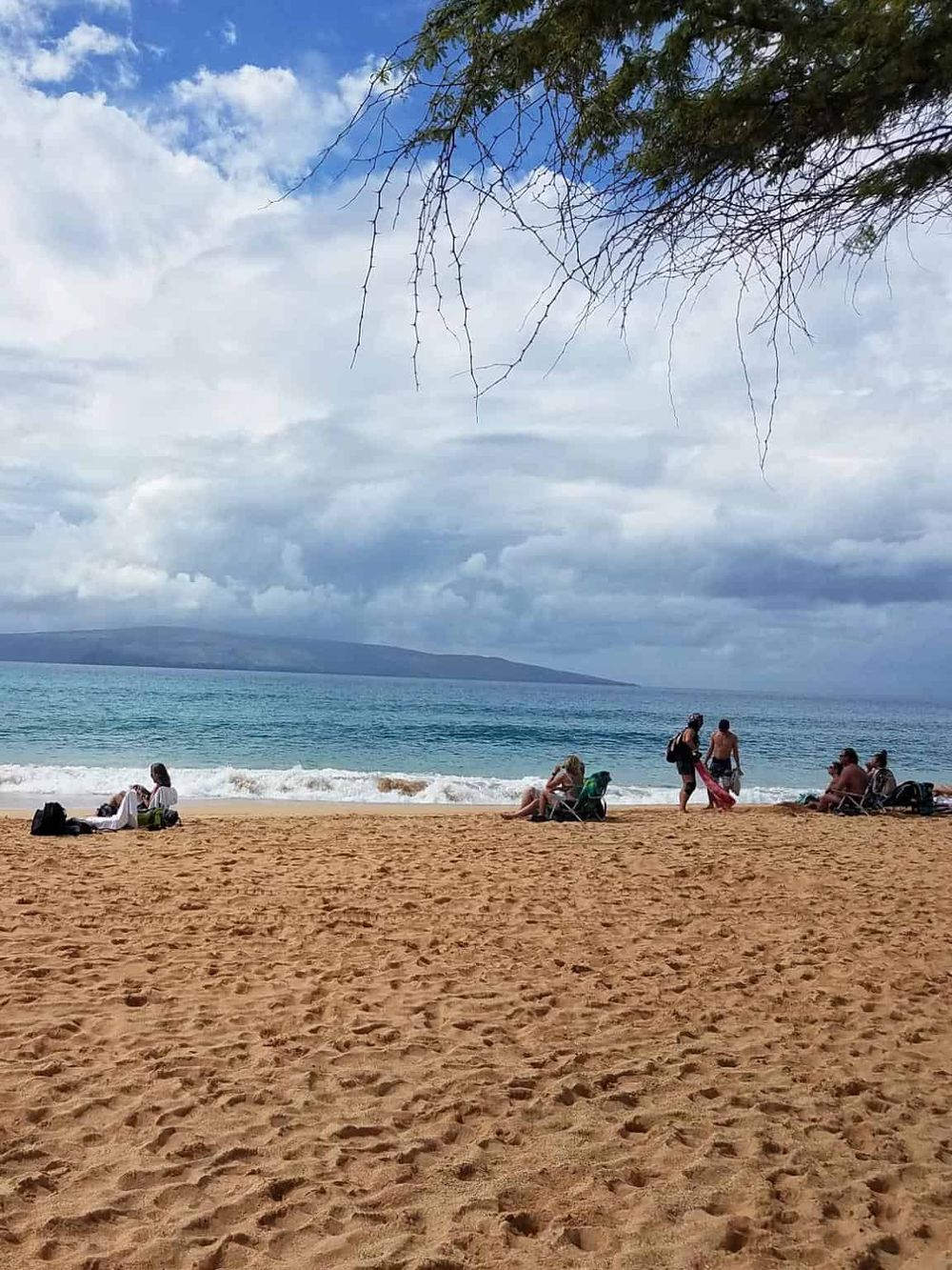 Relaxing Hawaii beach scene with tourists, blue ocean, and cloudy sky, perfect for travel inspiration.