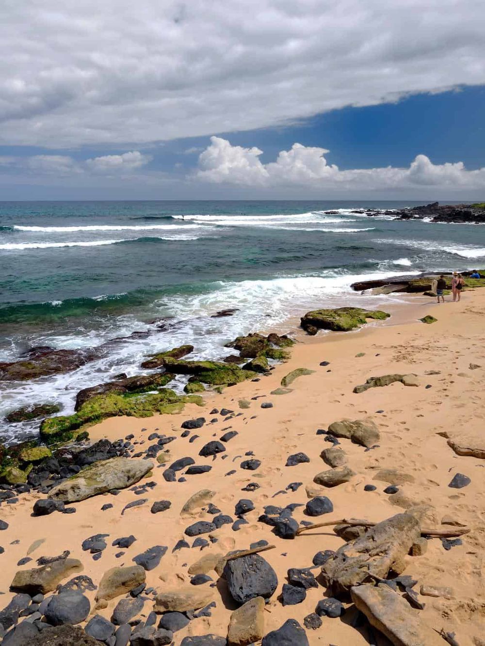 Calm ocean waves crashing on rocky sandy beach under partly cloudy sky, scenic coastal landscape.