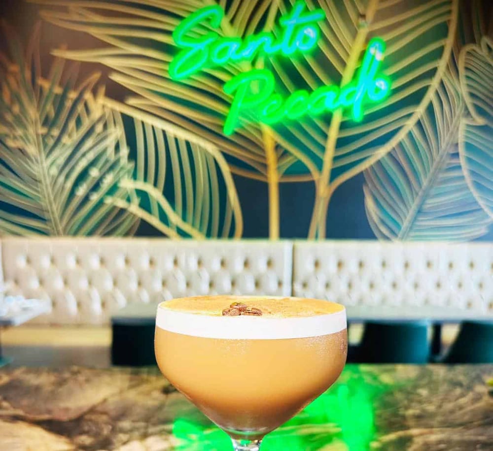 Neon "Eat & Relax" sign with tropical leaves in background, with a cocktail in foreground.