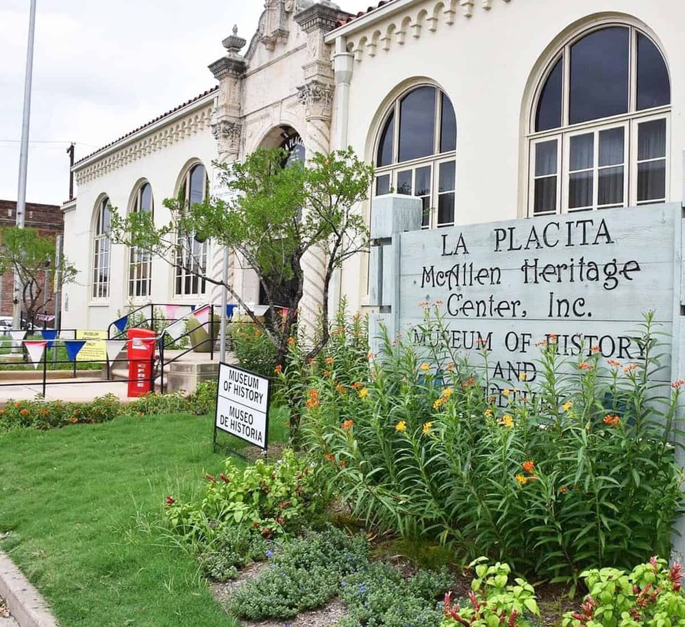 Historic museum building with lush greenery and welcoming signs for the Museum of History and La Placita Heritage Center.