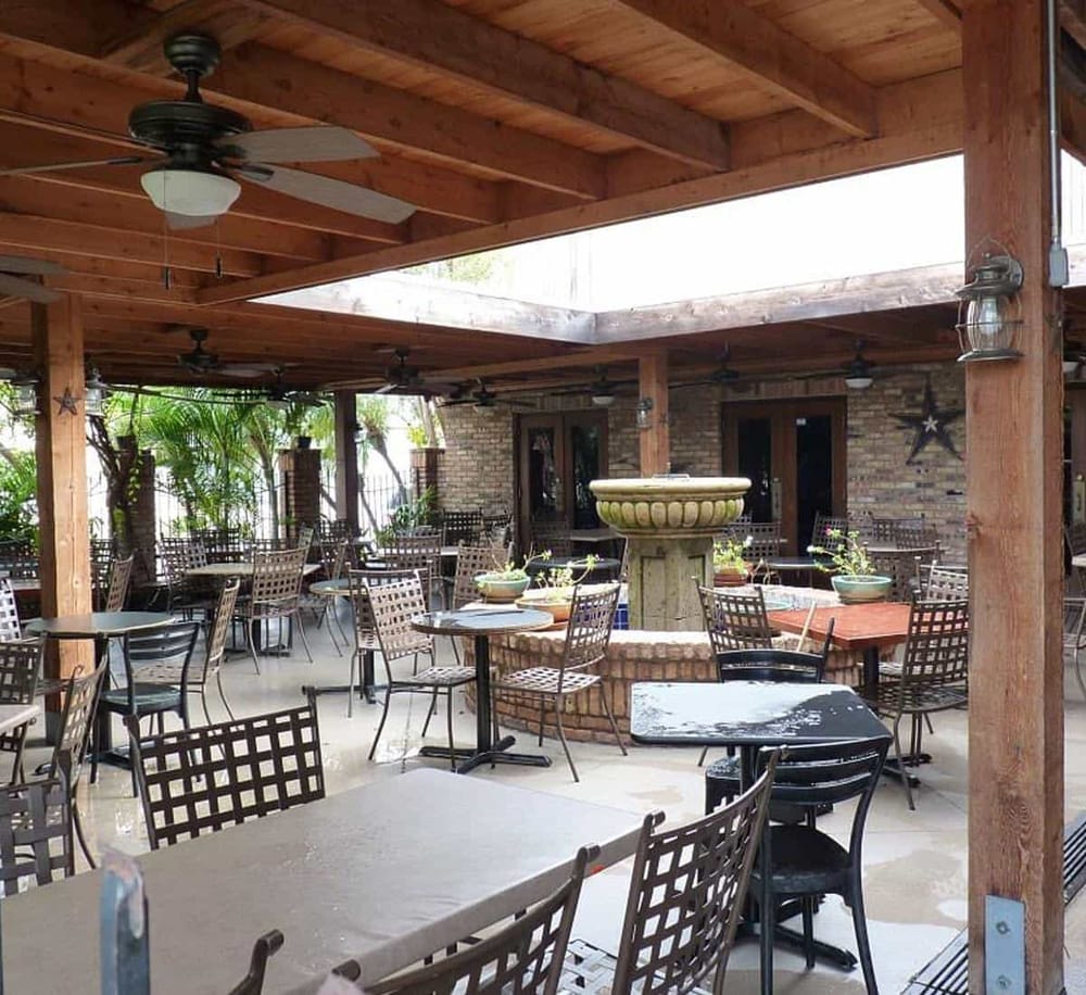 Spacious outdoor dining area with wooden beams, ceiling fans, and brick accents, perfect for restaurants or events.