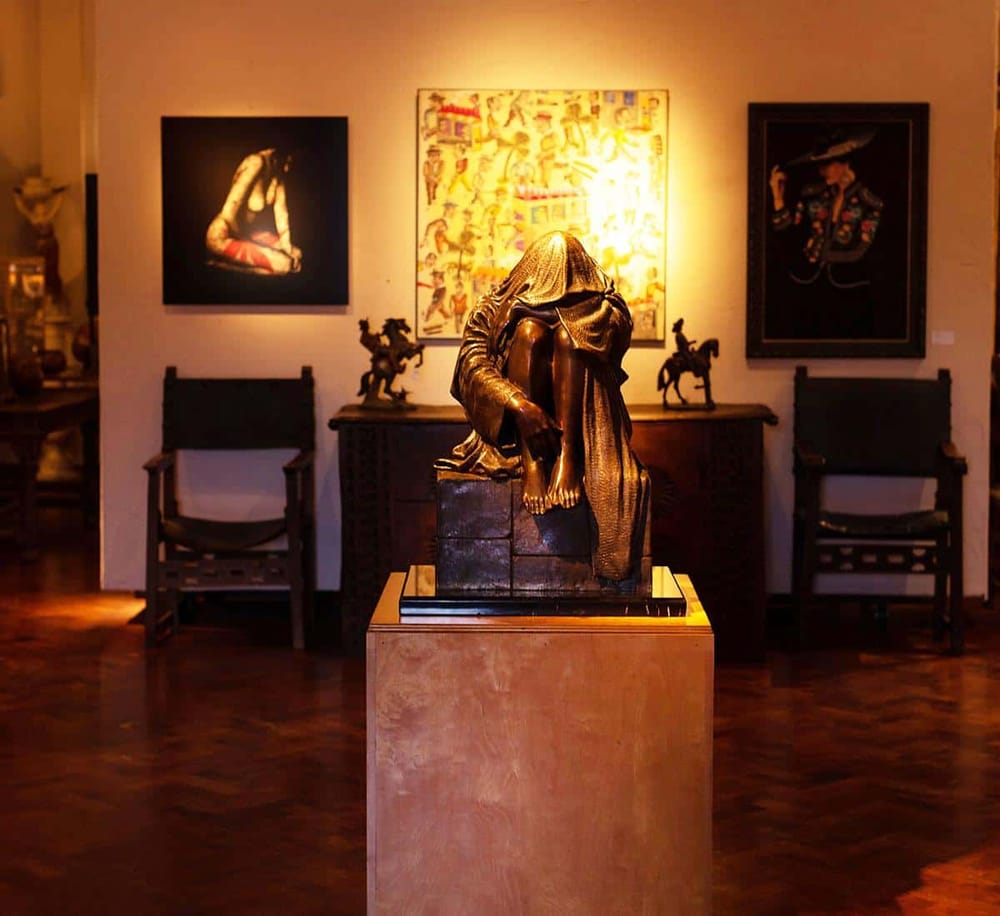 A bronze sculpture of a seated woman with a headscarf at an art gallery, illuminated by warm lighting.