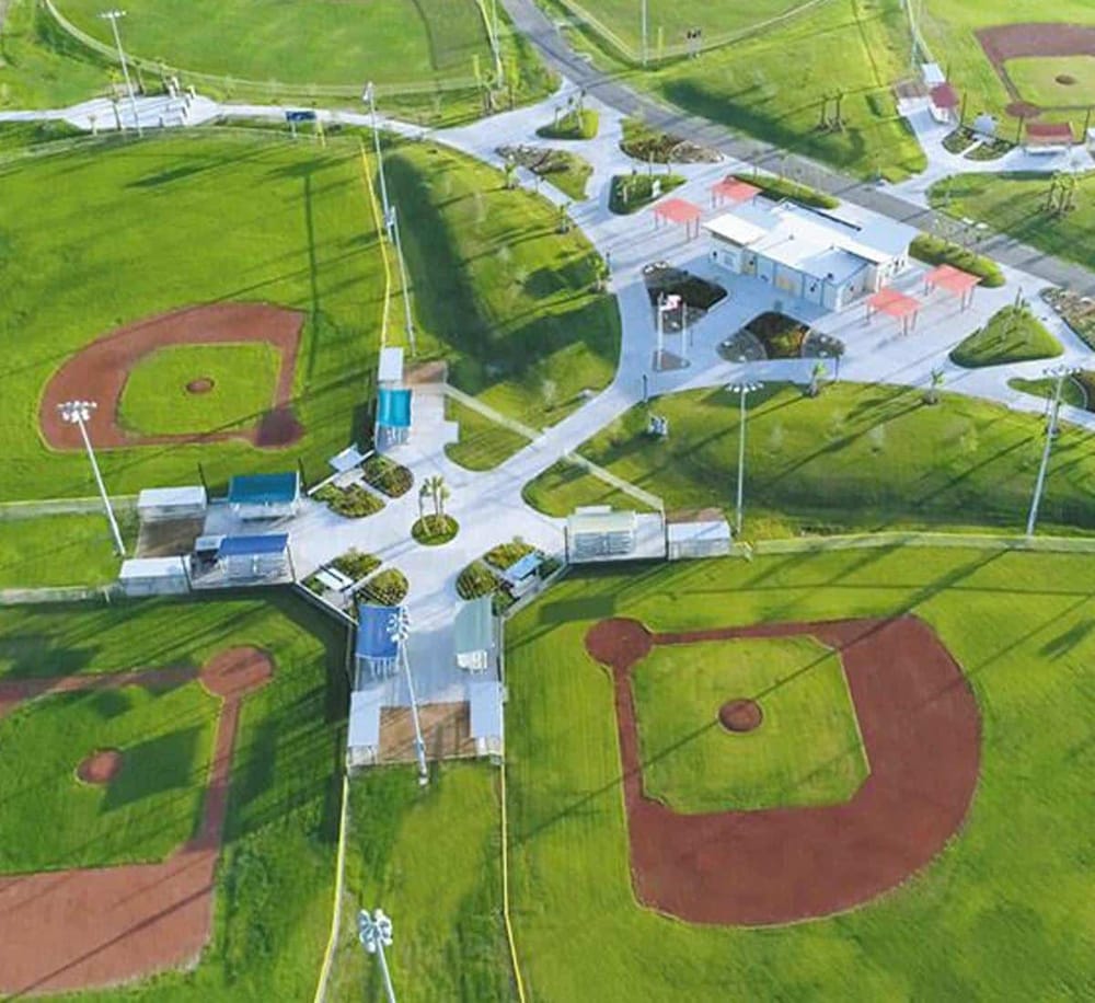 Bright aerial view of a community sports park with baseball fields, walking paths, and green spaces, showcasing outdoor recreational facilities.