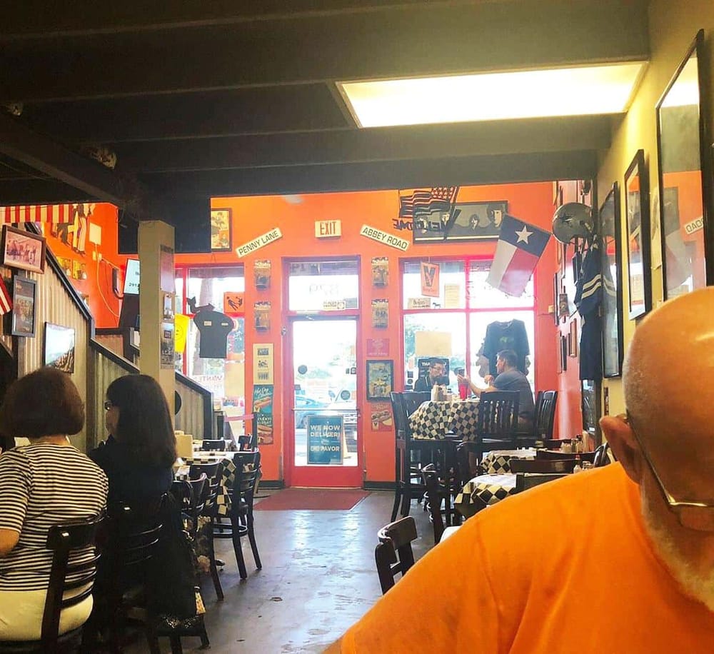 Colorful Texan-themed restaurant interior with vibrant decor, flags, and casual dining atmosphere, live sports on TV, and diverse customers.