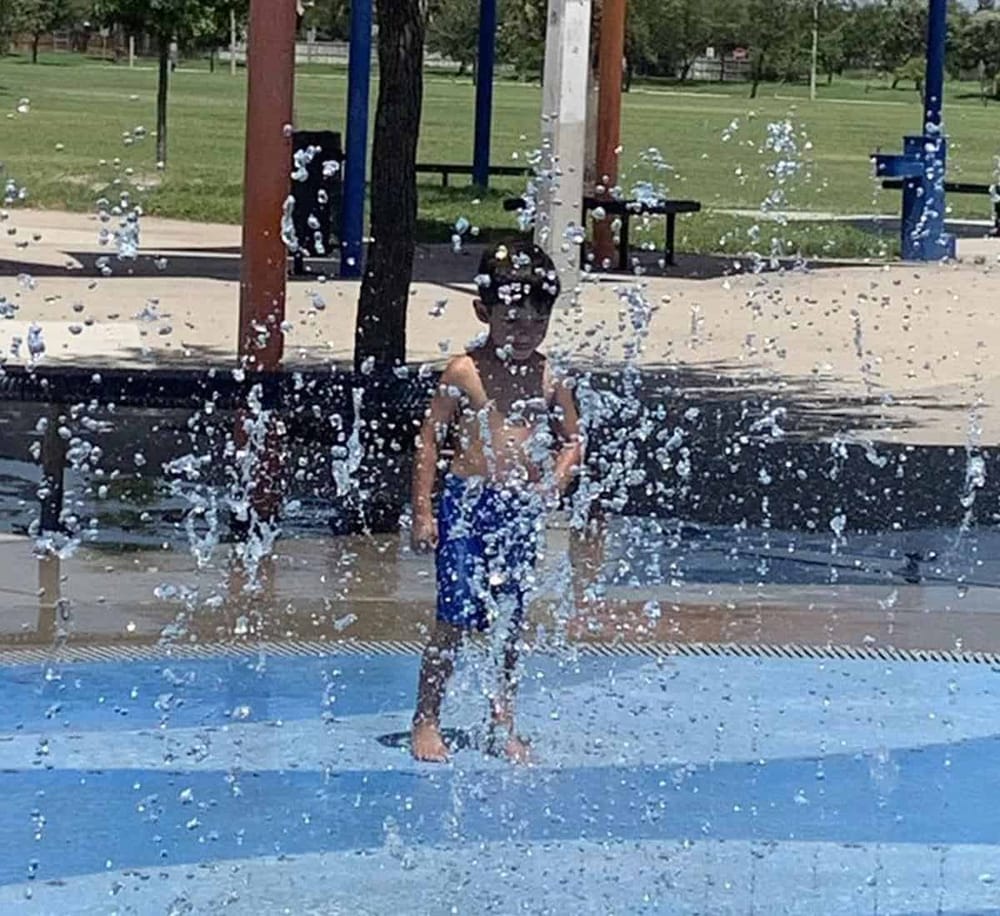 Kids playing in splash pad at park, summer outdoor water fun and recreation.
