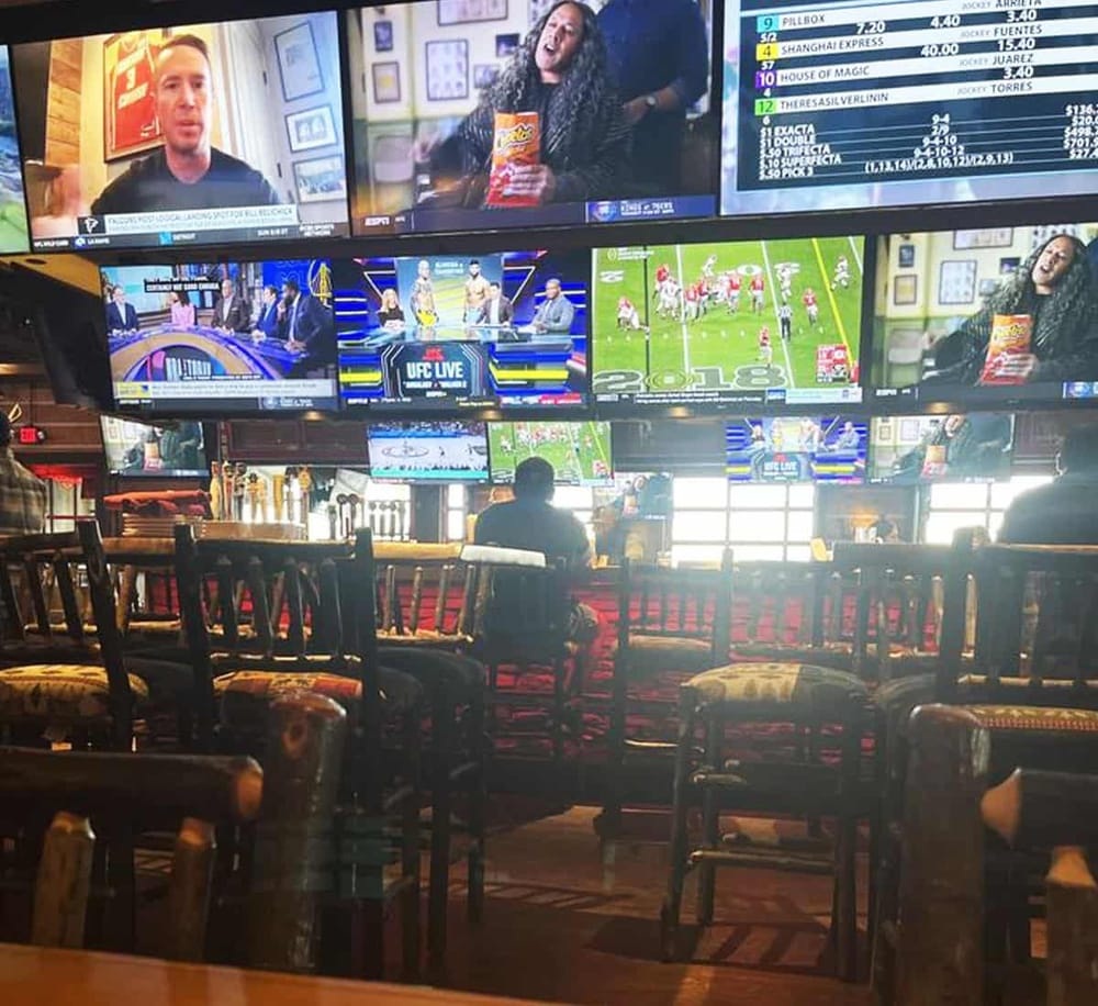 Bright sports bar with multiple TV screens showing live sports, betting odds, and news, creating a lively atmosphere for fans.