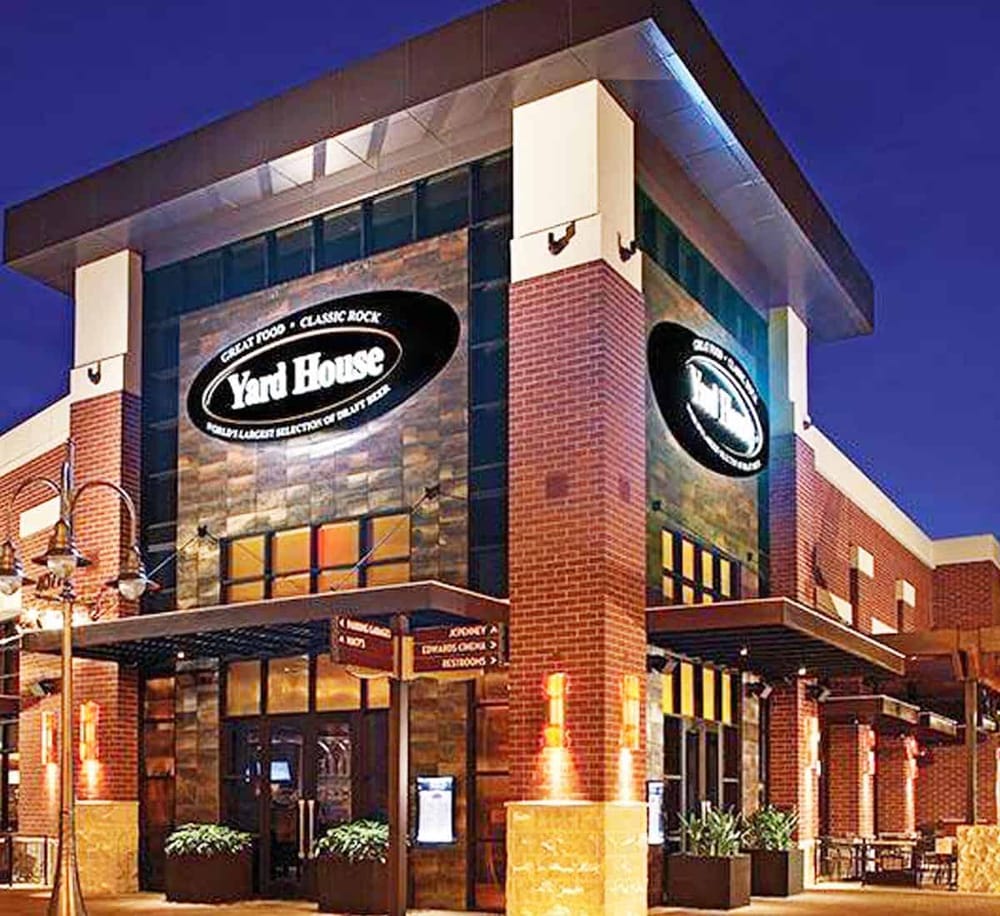 Modern restaurant exterior at dusk with illuminated sign for Yard House, a popular American chain serving craft beer and American cuisine.