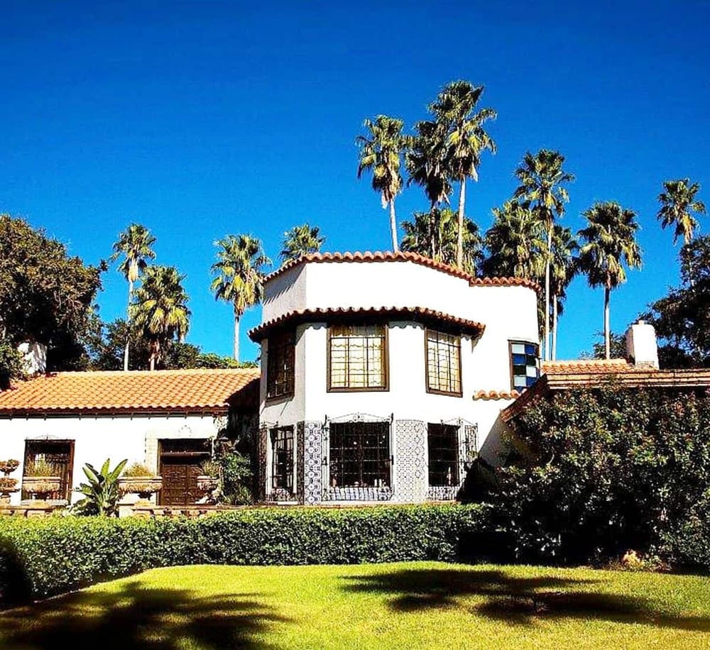 Colorful Spanish-style house with palm trees and lush garden under bright blue sky.