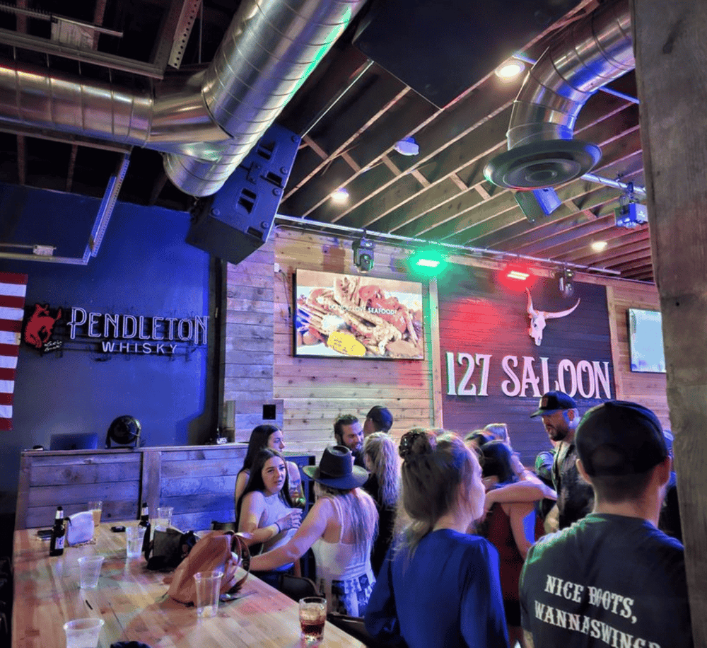 Vibrant bar and restaurant interior with group of patrons and neon signage at 127 Saloon.