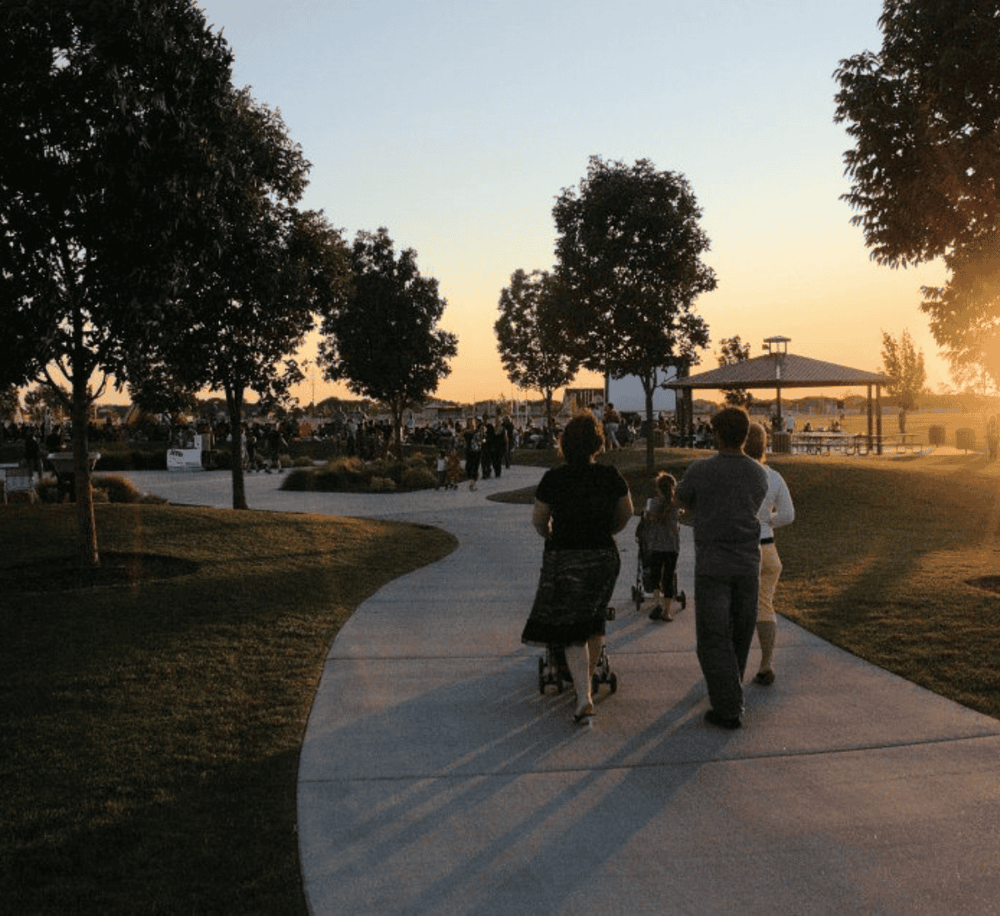 Families enjoying sunset at park with walking trail, trees, and open pavilion for outdoor recreation.