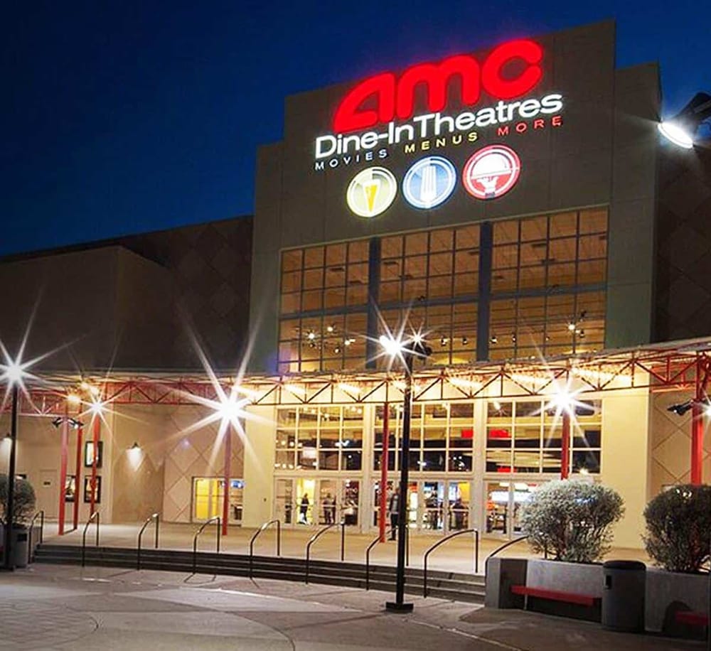 AMC theater at night with illuminated signage for movies, food, and dining options.