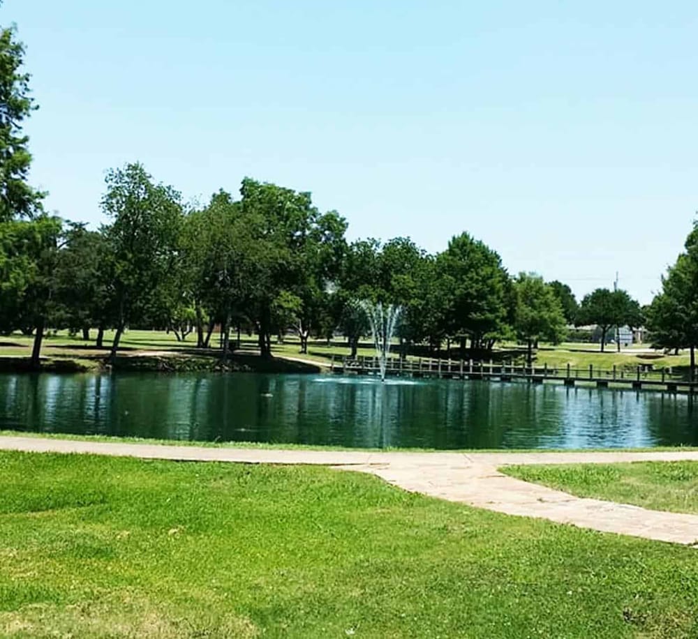 Tranquil park with pond, fountain, and lush trees, ideal for walking and outdoor relaxation.