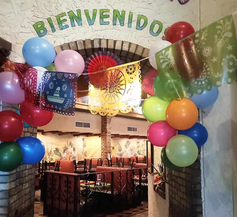 Colorful balloons and papel picado decorations at a festive celebration entrance.