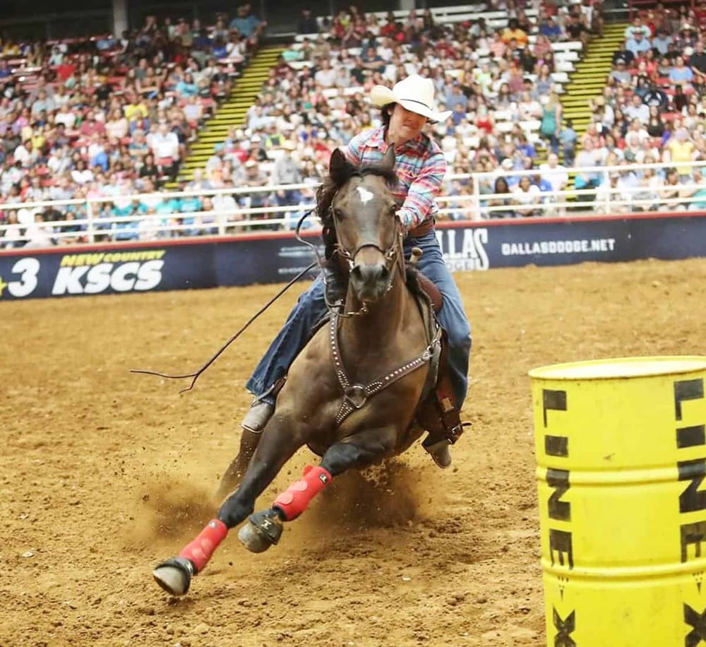 Fast-paced rodeo event with rider navigating around barrels on a spirited horse.