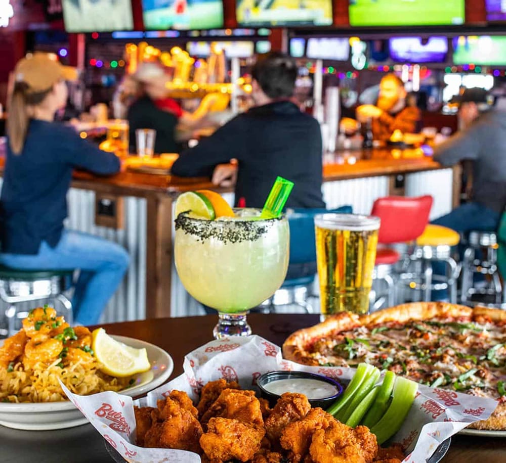 Bright drinks and classic American comfort food at a lively bar with sports on TVs in the background.