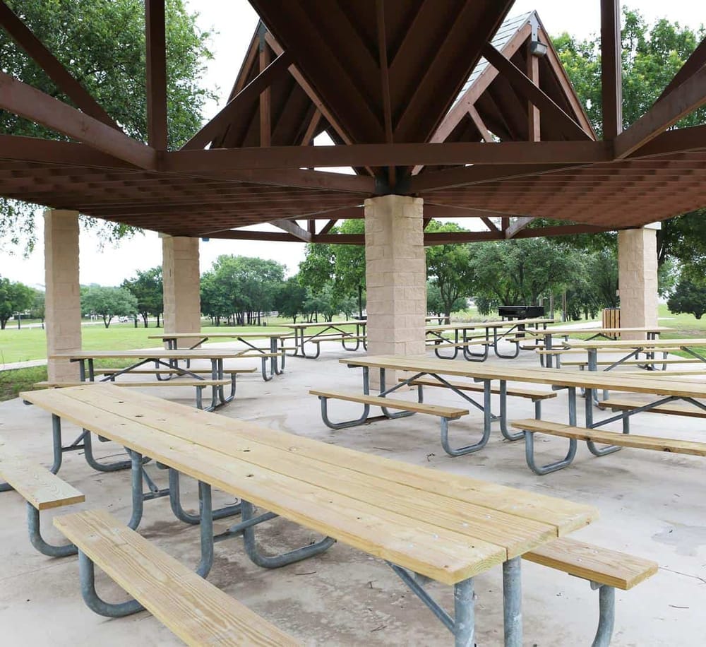 Covered park pavilion with picnic tables and lush green trees in the background.