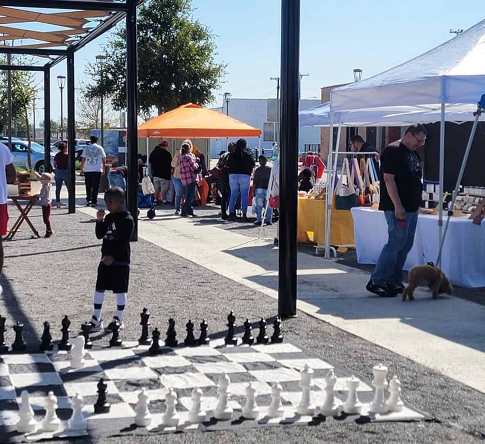 Colorful outdoor marketplace with vendor tents and shoppers, showcasing community events and local crafts.