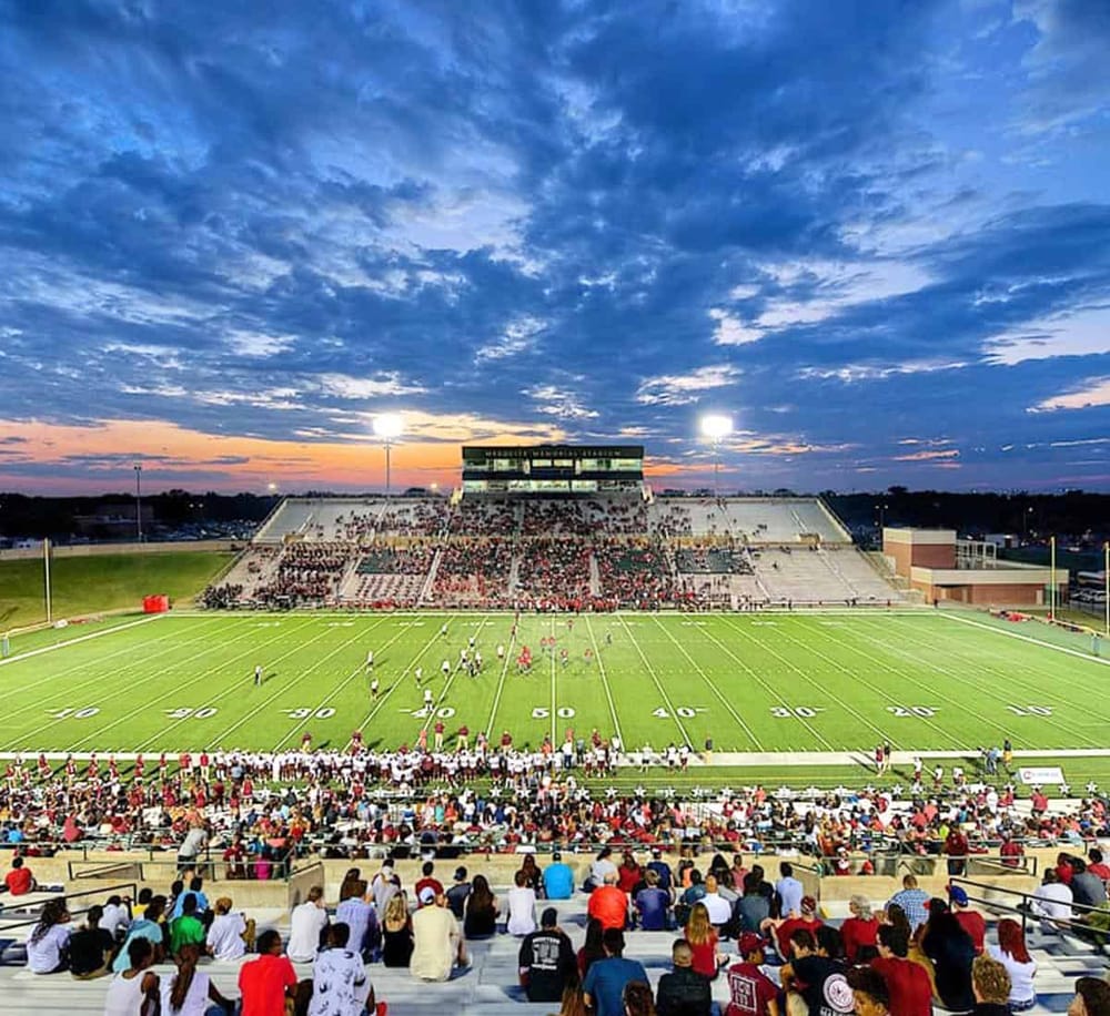 Stadium football game at sunset with cheering crowd and vibrant sky.