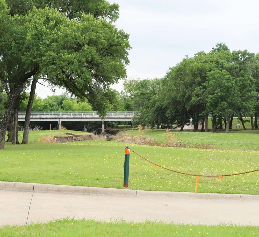 Lush green park with trees and a walking path near a bridge, ideal for outdoor activities and nature walks.