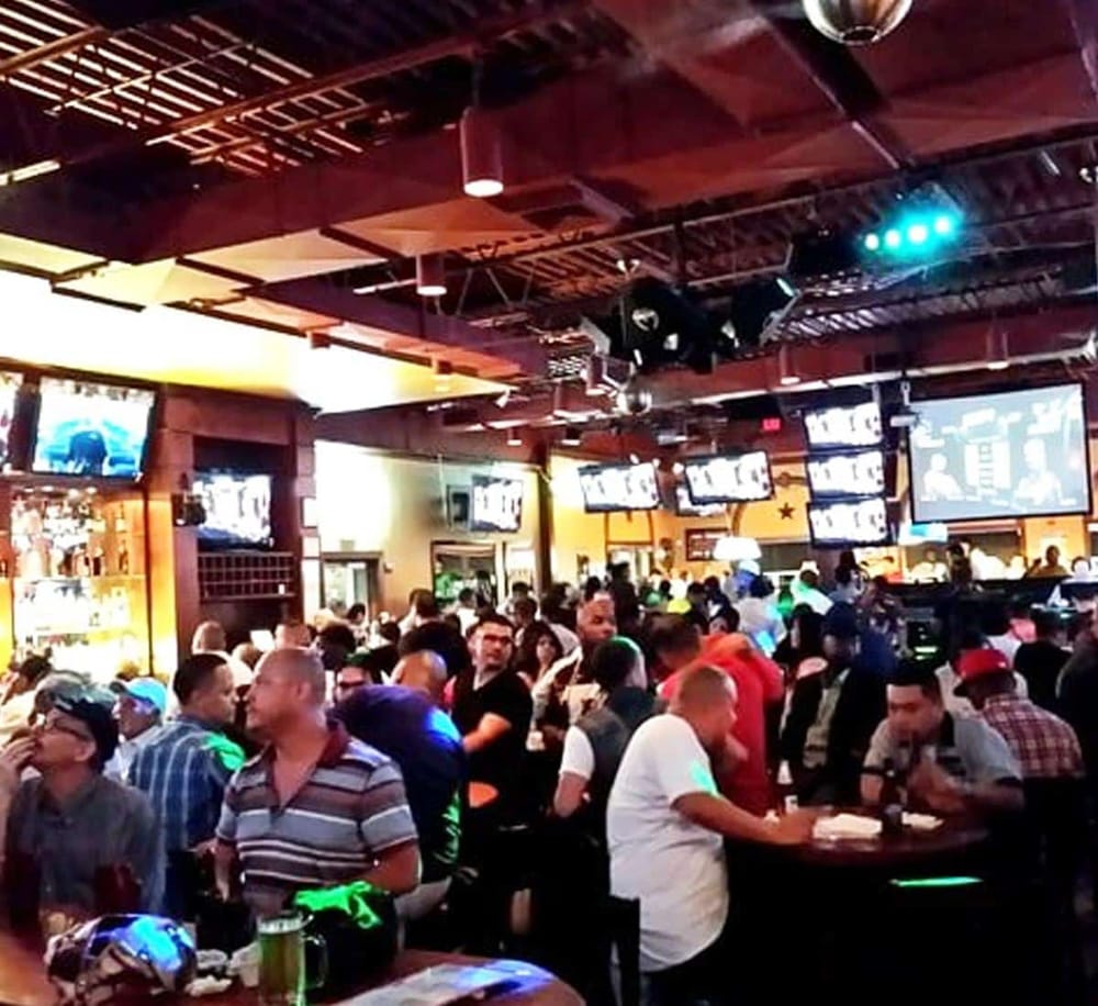Crowd at sports bar with multiple TV screens, lively atmosphere, and neon lighting.