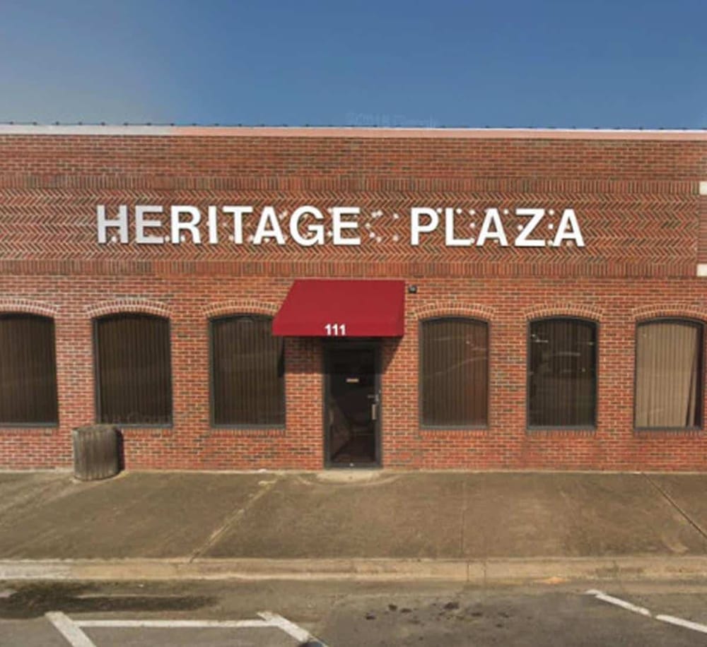 Heritage Plaza brick building with red awning, property signage, and office windows.