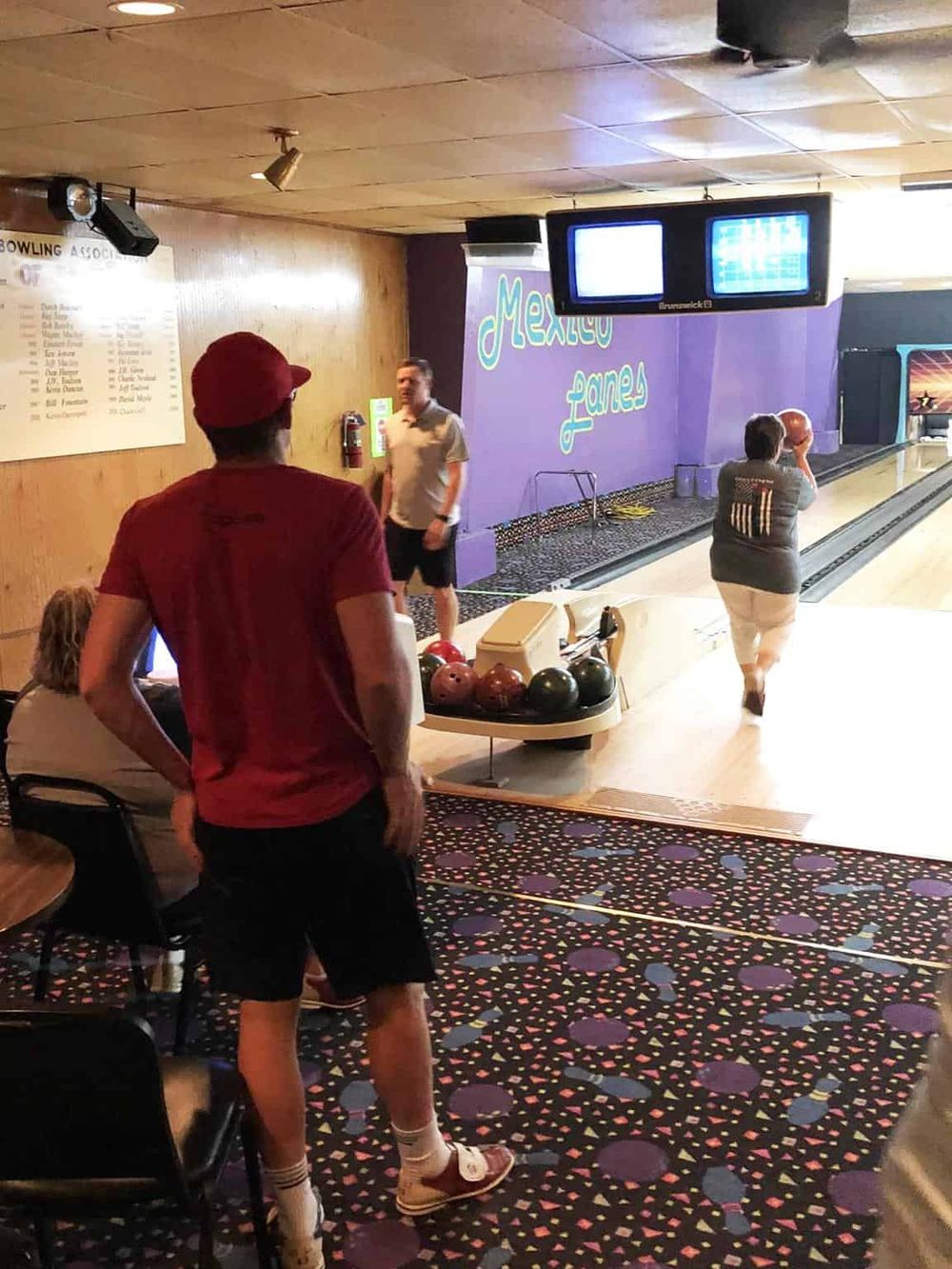 People playing bowling at Quest for Directions entertainment center, featuring colorful decor and league scoreboard.