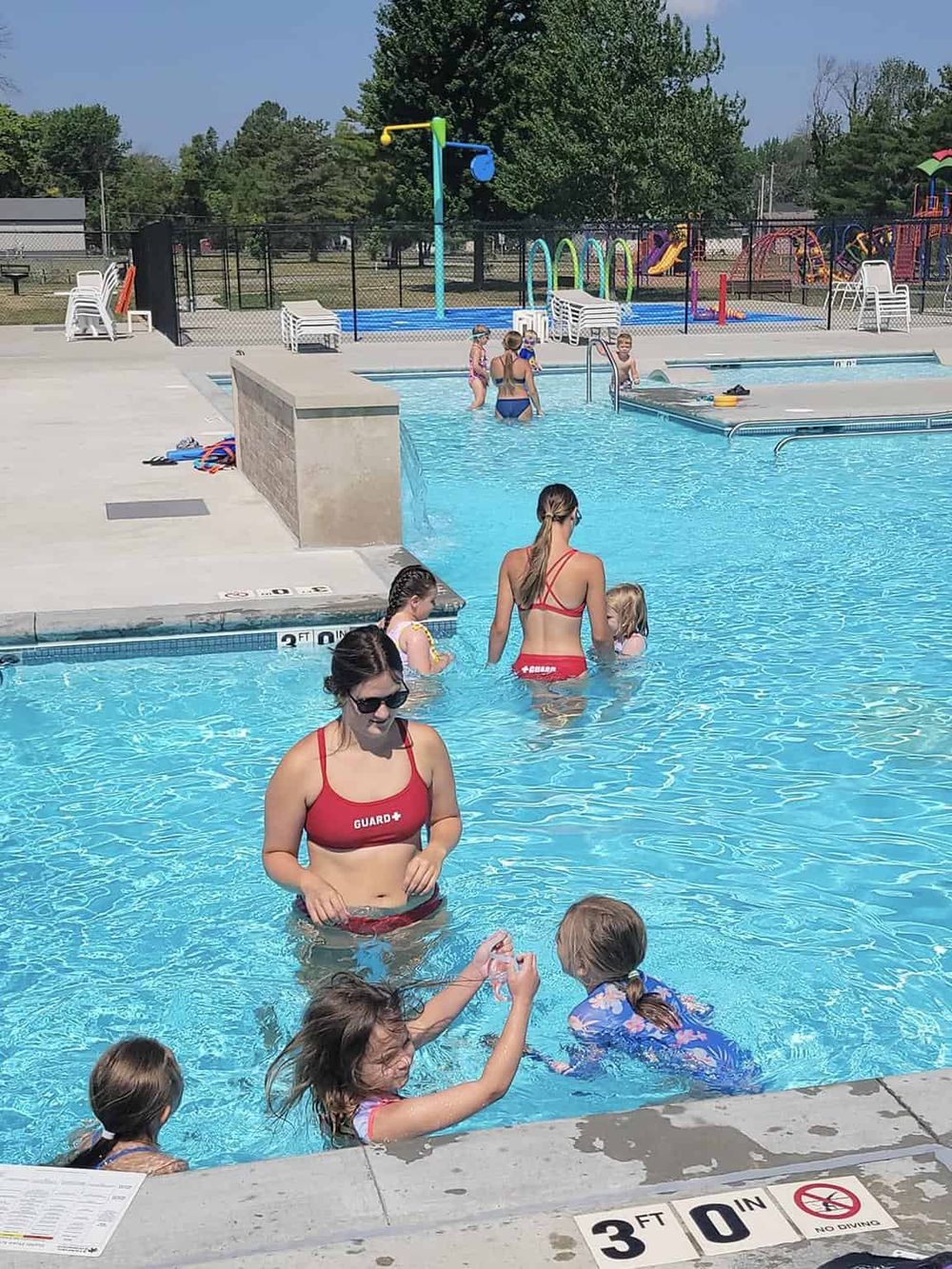 Bright summer swim safety at QUEST FOR DIRECTIONS community pool, featuring lifeguards and children enjoying water activities.