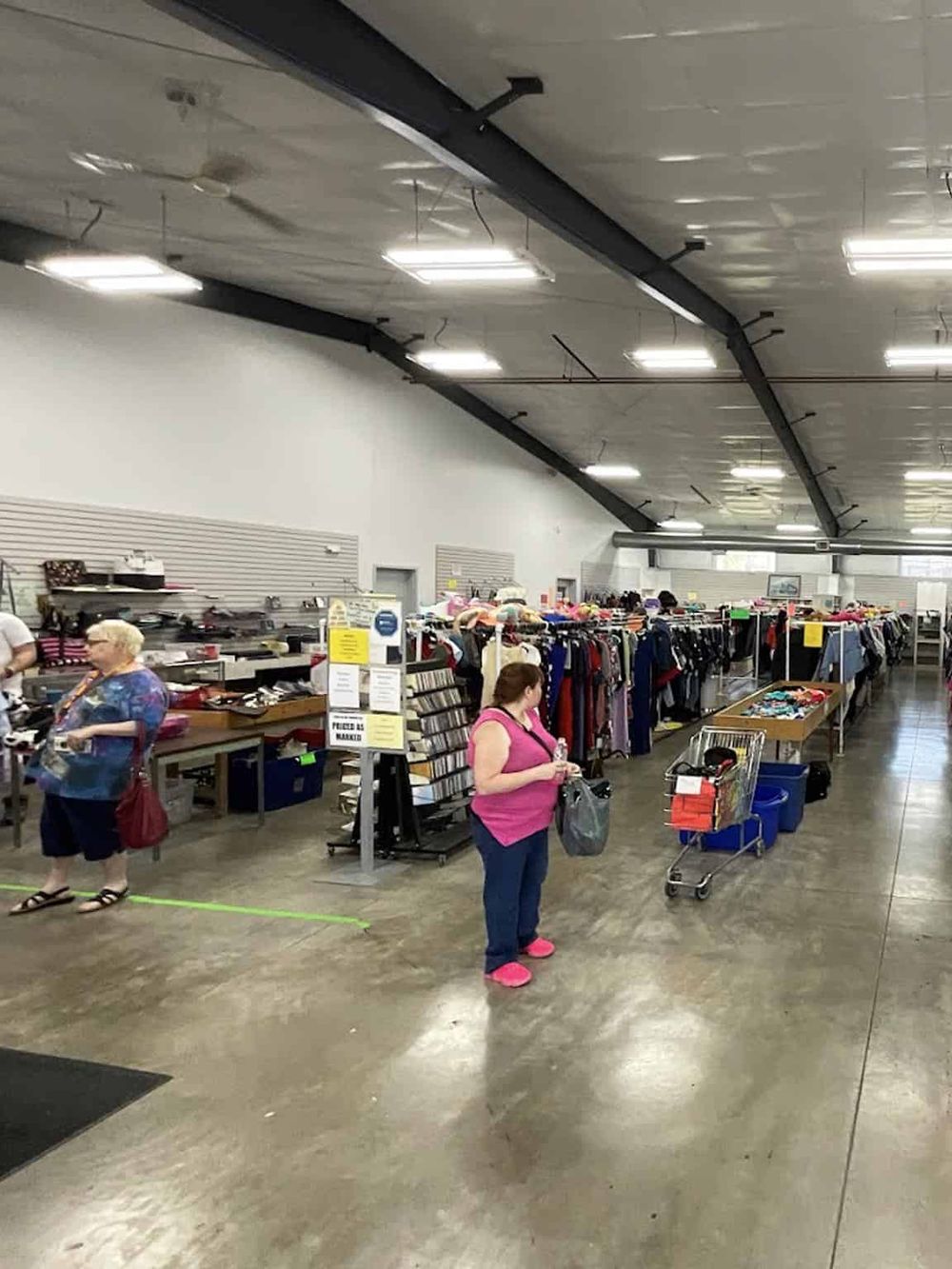 Aisle of thrift store with shoppers browsing clothing and accessories for affordable deals.