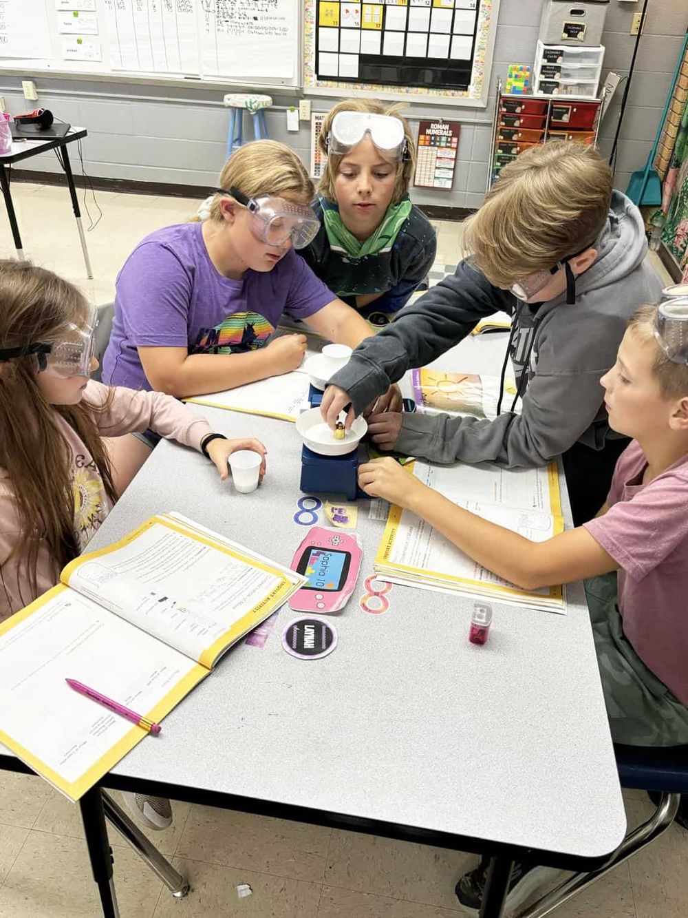 Youth science experiment in classroom, students wearing goggles, engaging in hands-on learning.
