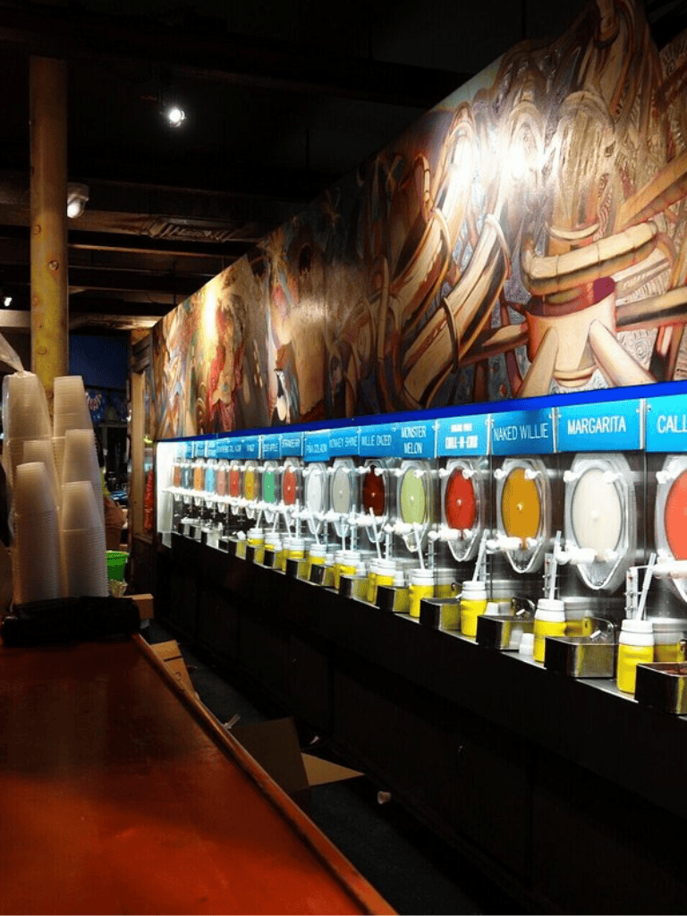 Freshly made juice dispensers at QuestForDirections beverage station with colorful murals in background.