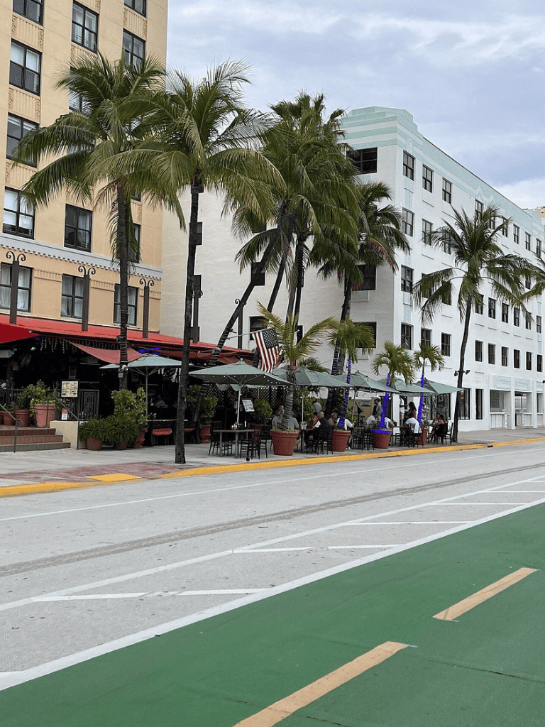 Outdoor cafe with palm trees and colorful umbrellas in a city street setting.